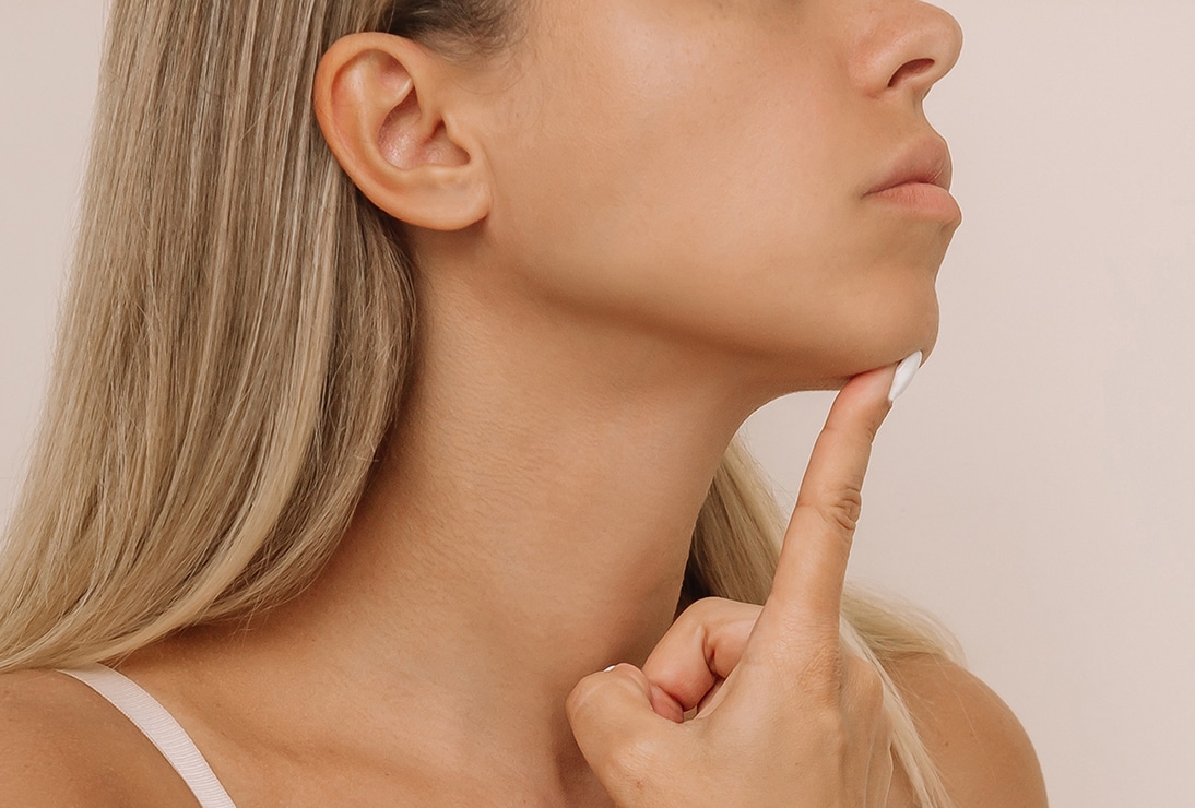 Woman pointing to her chin, highlighting jawline and neck.